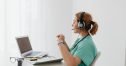 A female doctor using a laptop for an online consultation, wearing a headset in a bright office.